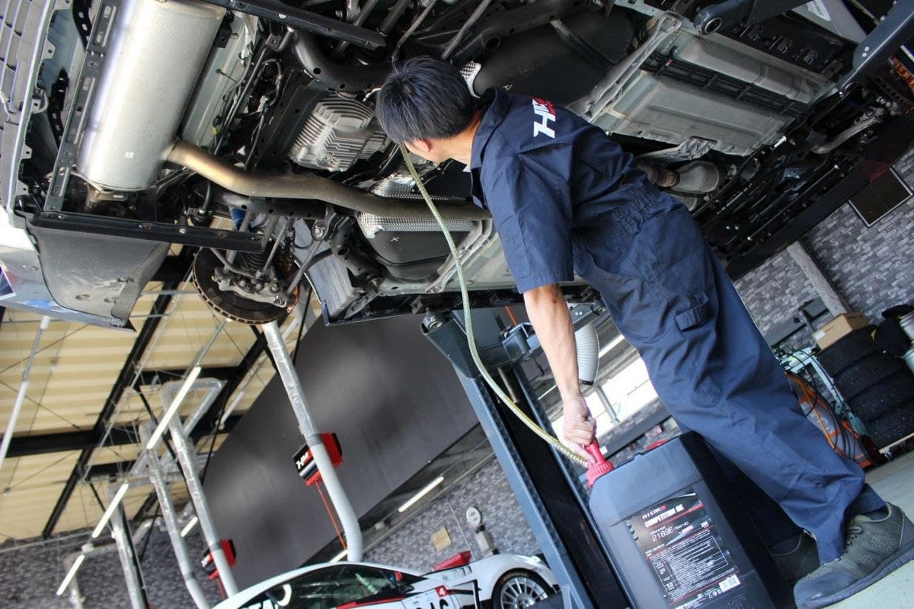HM-R technician inspecting the undercarriage of a vehicle on a workshop lift